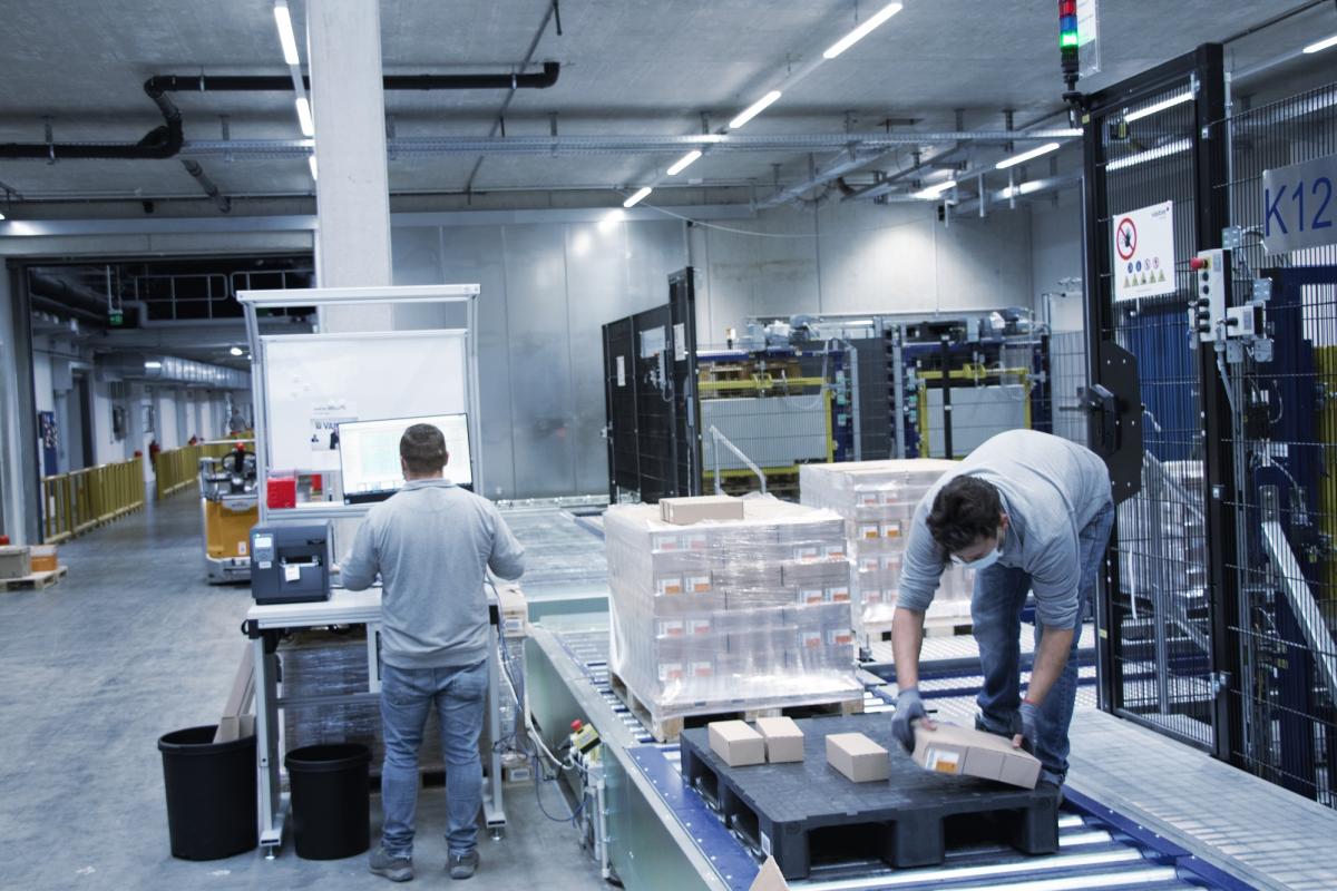 Two employees at the goods-to-person picking station in the viastore high-bay warehouse at VARTA in Ellwangen 
