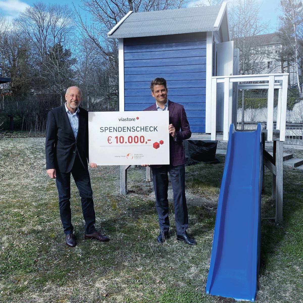 Philipp Hahn-Woernle, CEO von viastore, überreicht vor blauer Kinderrutsche Spendenscheck an Stefan Nägele im Garten vom Blauen Haus