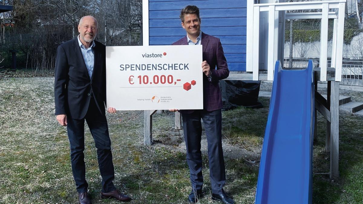 Philipp Hahn-Woernle, CEO von viastore, überreicht vor blauer Kinderrutsche Spendenscheck an Stefan Nägele im Garten vom Blauen Haus